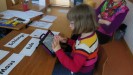 Das Foto zeigt eine Schülerin beim Lesen und Schreiben mit Wortkarten und iPad.