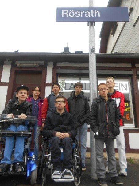 Das Foto zeigt sieben Schülerinnen und Schüler der LVR-Schule am Königsforst unter dem Bahnhofsschild von Rösrath.