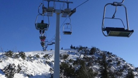 Auf dem Bild sieht man den Sessellift bei schönem Wetter hoch über den schneebedeckten Bergen.
