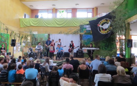 Die Band steht in der Schule auf der Bühne, die wie ein Wald dekoriert ist, und macht vor Publikum Musik.