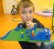 Auf dem Bild sieht man einen Schüler, der auf seiner Lego-Platte alles in Blautönen gebaut hat und diese strahlend in der Hand hält.