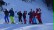 Auf dem Bild sieht man mehrere Schülerinnen und Schüler mit dem Skilehrer und mit Skiern in einer Reihe mitten im Skigebiet stehen.