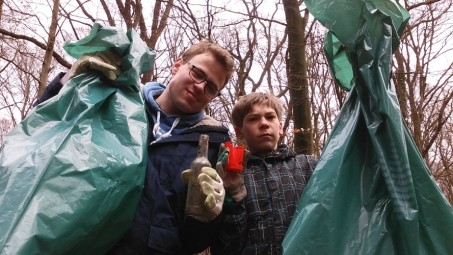 Zwei Schüler mit gefüllten Müllbeuteln und verschiedenen Fundstücken im Wald