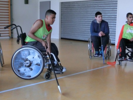 Drei Schüler im Rollstuhl spielen Hockey.