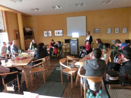 Schülerinnen und Schüler, Angehörige und Lehrkräfte bei einer Beamer-Präsentation im Schul-Café.