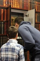 Foto: Zwei Schüler stehen mit dem Rücken zugewandt vor einem Tresor gebeut vor einer Bücherwand
