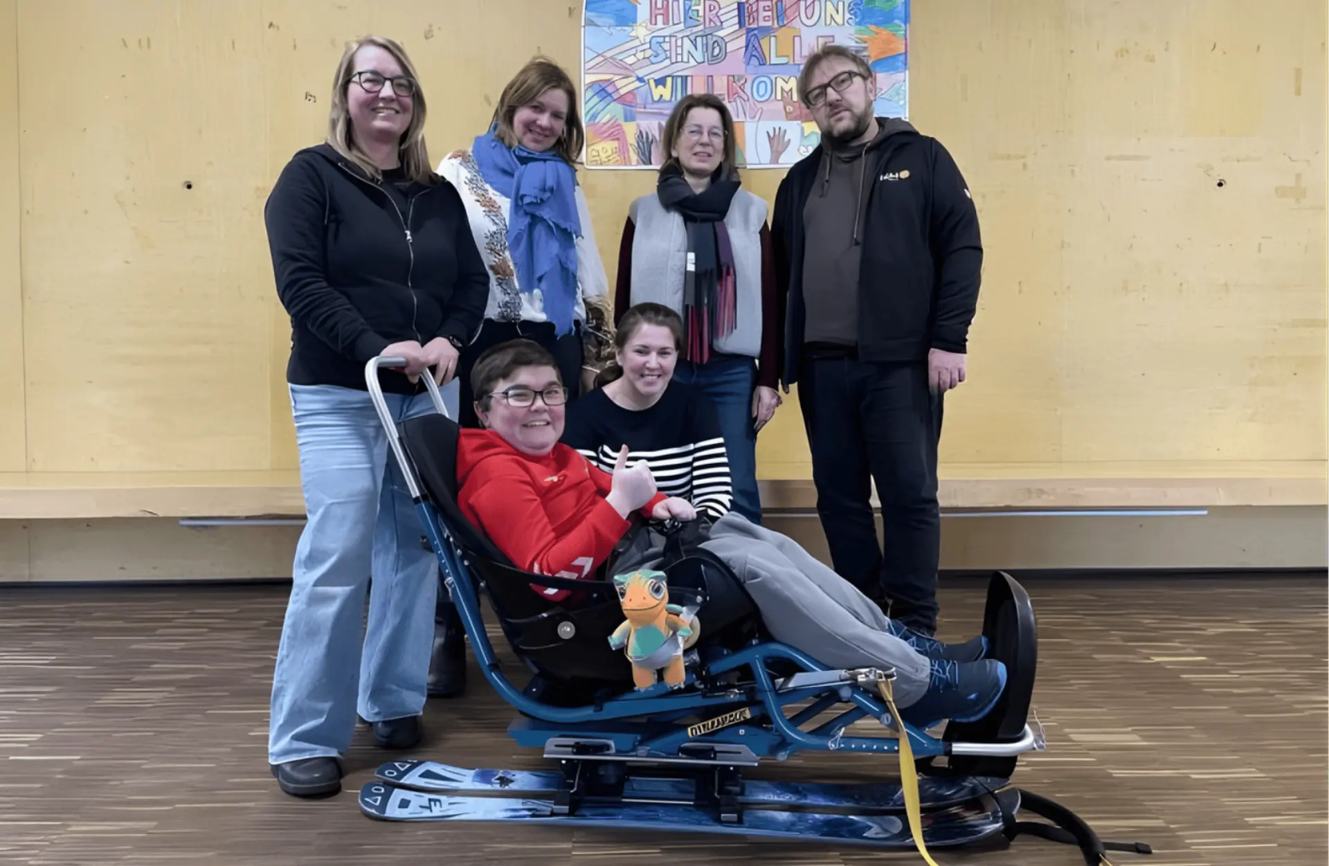 Der neue Skibob mit seinem ersten Skifahrer und dem Maskottchen von KiNiKi, den Spender*innen, der Schulleitung und Lehrerinnen vom Skiteam der Schule